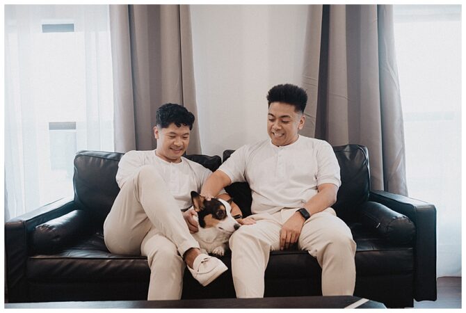 Two men on sofa with a happy dog.