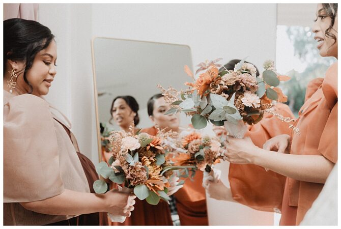 Bridesmaids holding orange floral bouquets inside room.