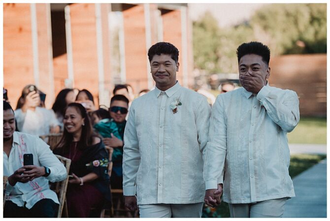 Two grooms walking down aisle, holding hands